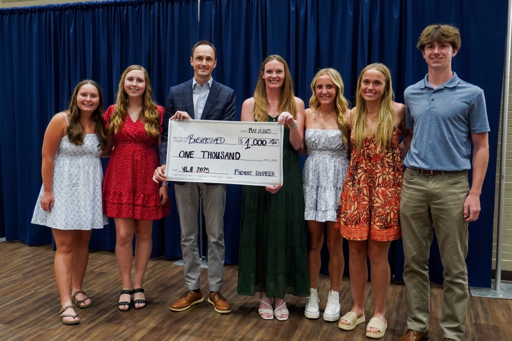 students gathered with organizer who is holding up an oversized check for $1000